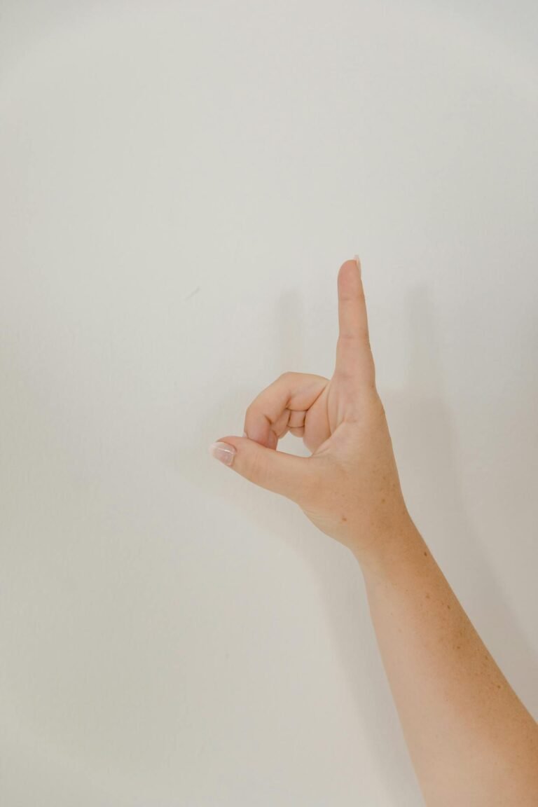 A woman's hand creating a sign language gesture against a plain white background, offering clear copy space.