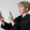 Asian woman gesturing with hands, demonstrating sign language on a white background.